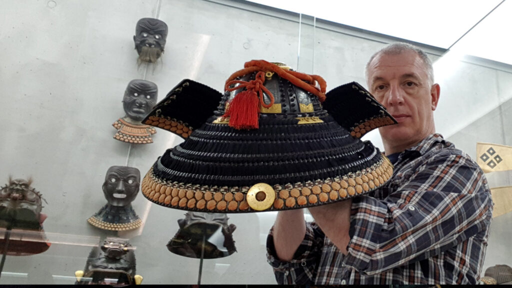 Close up portrait of David Thatcher holding a restored Japanese kabuto helmet prepared for the Samurai Art Museum Berlin